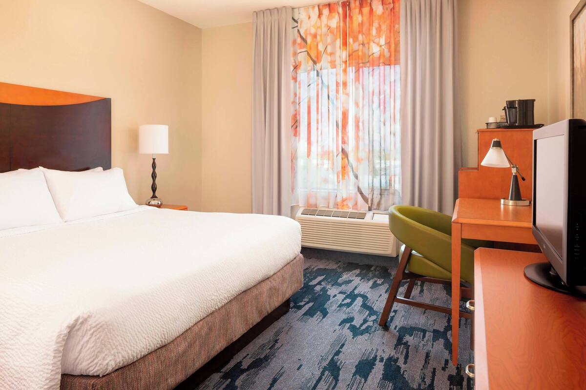 Une chambre d’hôtel équipée d’un lit, d’un bureau, d’une chaise, d’une télévision, d’une lampe et d’une fenêtre avec des rideaux.