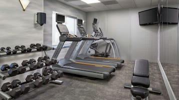 A gym with treadmills, dumbbells, and a bench.