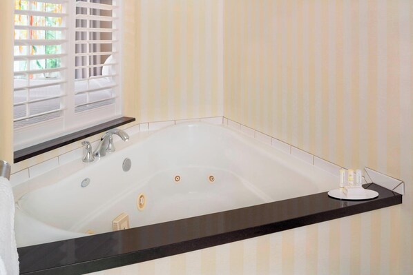 A modern bathroom with a freestanding bathtub, a black countertop, and a window with blinds.
