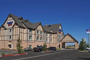 Un hotel con fachada de estilo Tudor, varios espacios de estacionamiento y un cielo azul despejado.