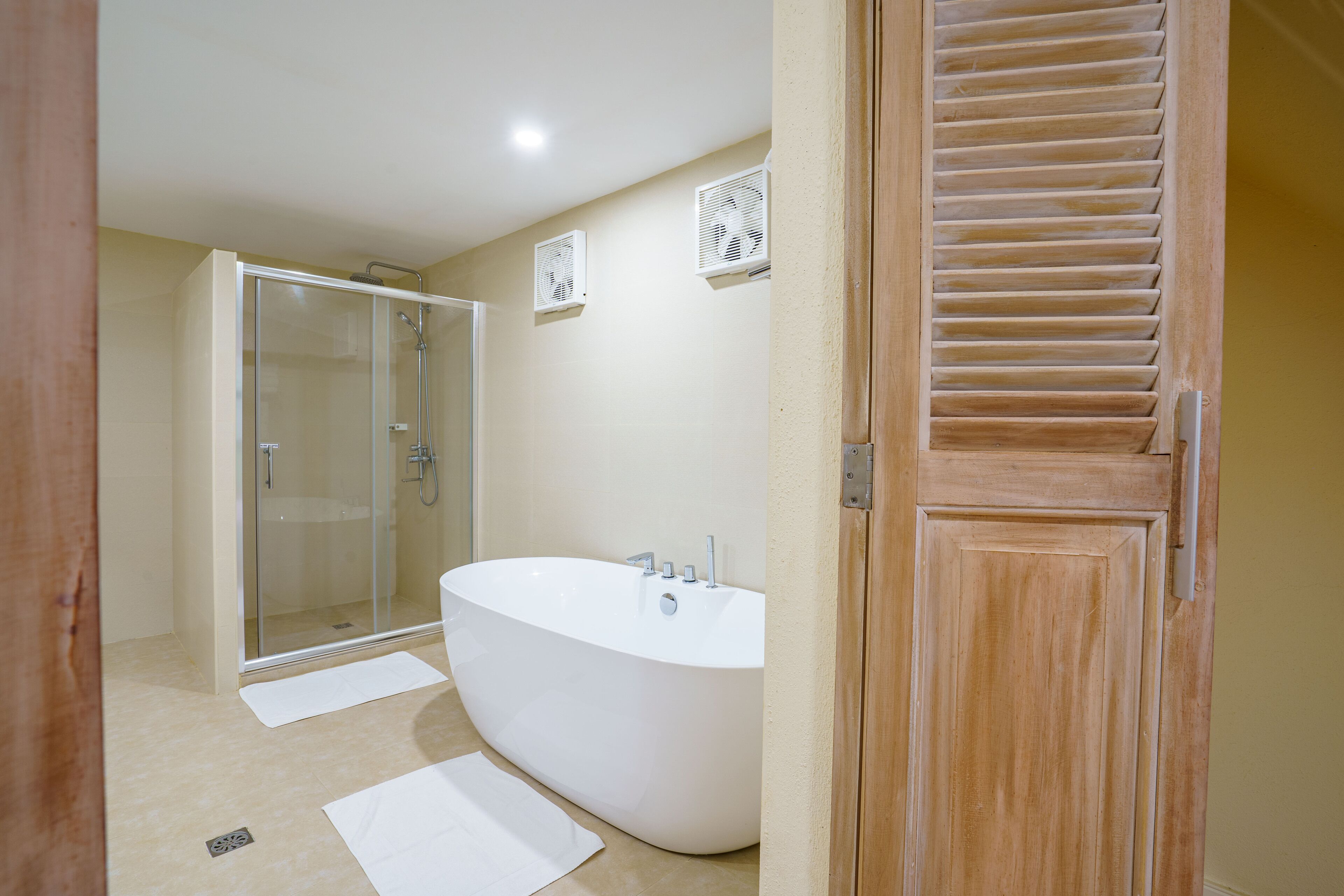 A modern bathroom with a glass-enclosed shower, a freestanding bathtub, and a wooden door.