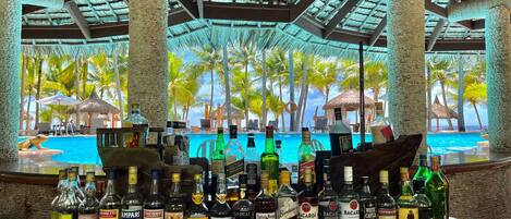 A bar with a tropical view, featuring a variety of liquor bottles and a poolside setting.