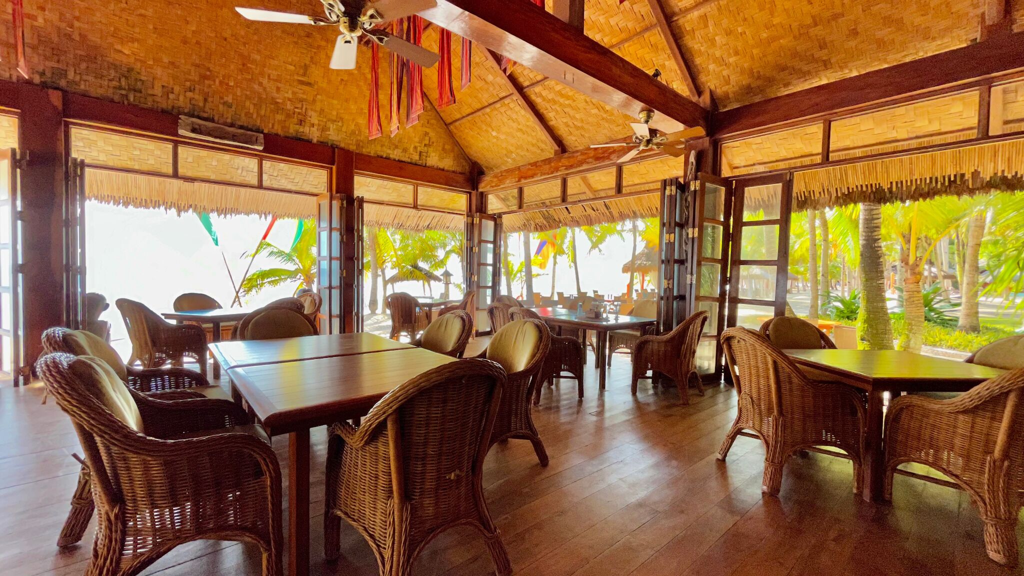 An open-air dining area with wicker furniture and a thatched roof.