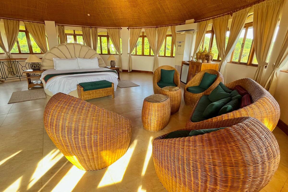 A spacious room with a large bed, wicker furniture, and large windows with curtains.