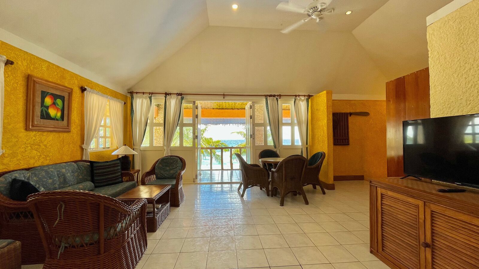 A spacious living area with a sofa, dining table, and chairs, a television, and a view of the ocean.