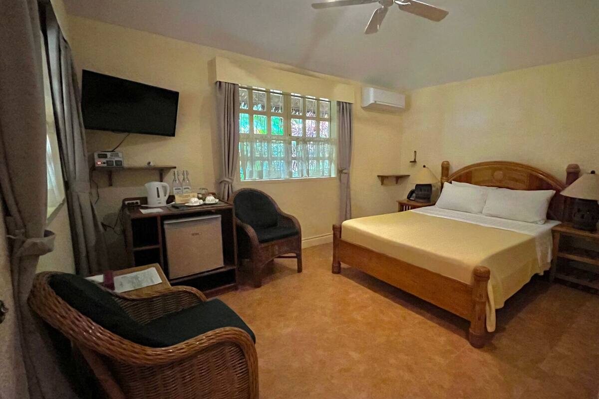 A bedroom with a bed, a desk, a chair, a television, and a window with curtains.