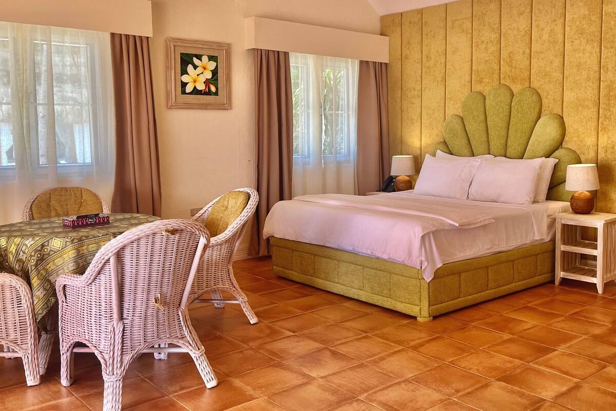 A hotel room with a large bed, a dining table with chairs, and a picture of flowers on the wall.