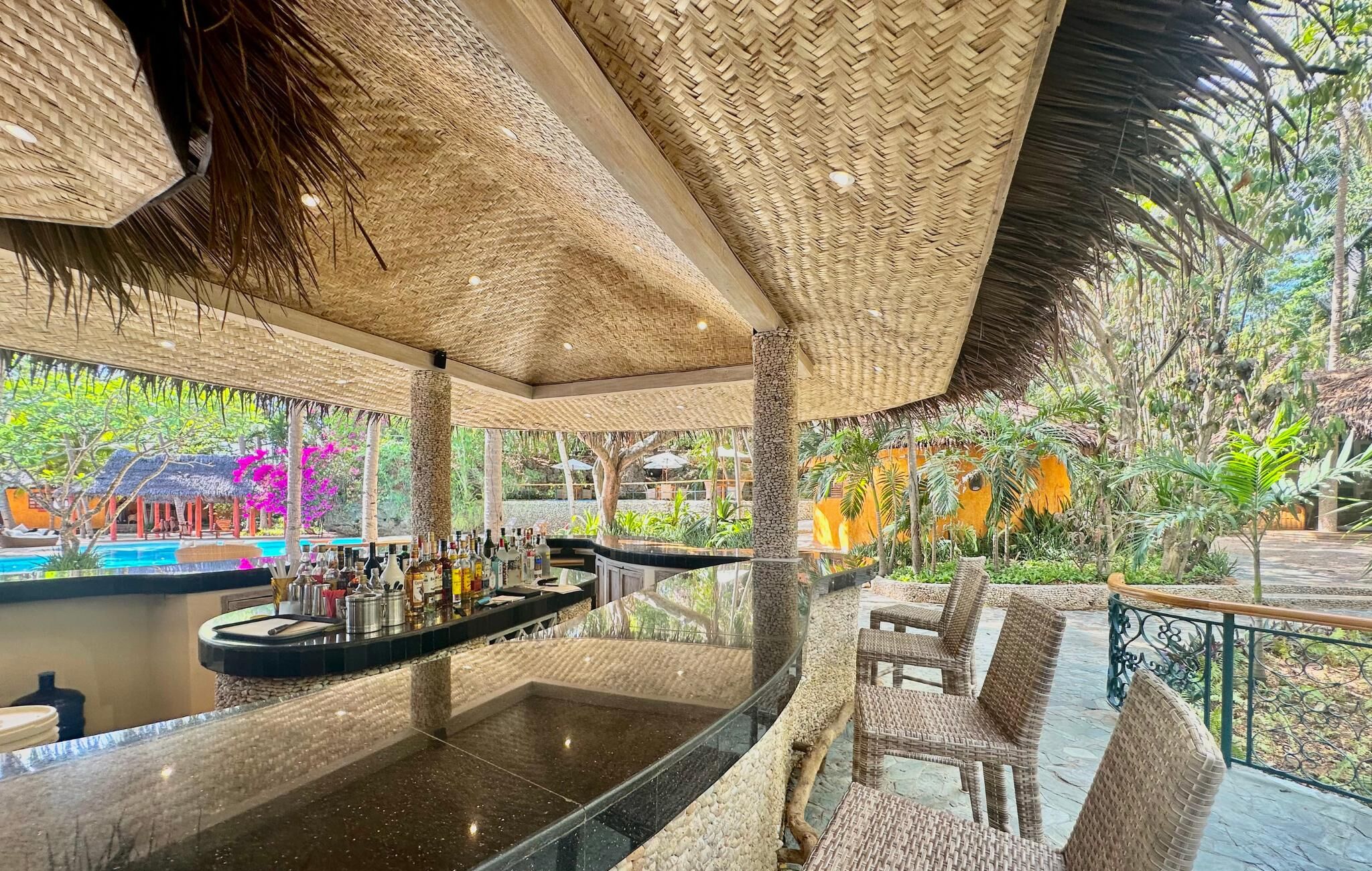 A bar area with a pool view, wicker furniture, and tropical plants.