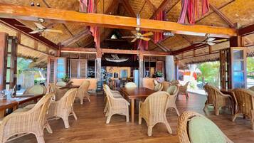 A spacious indoor area with wooden flooring, wicker furniture, and a thatched roof.
