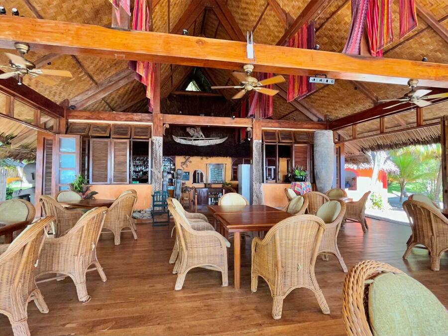 A spacious indoor area with wooden flooring, wicker furniture, and a thatched roof.