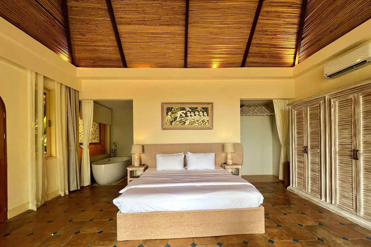 A spacious bedroom with a large bed, a bathtub, and a wardrobe.