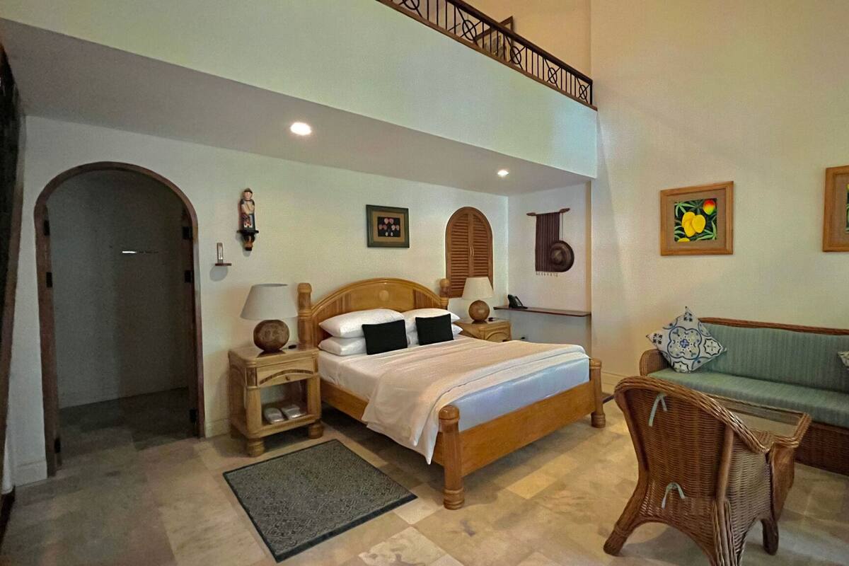 A bedroom with a wooden bed, nightstands, a wicker chair, a sofa, and a staircase.