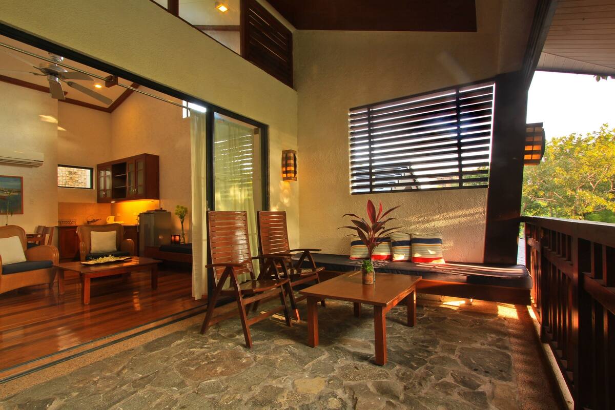 A spacious living area with a stone floor, wooden furniture, and a large window with blinds.