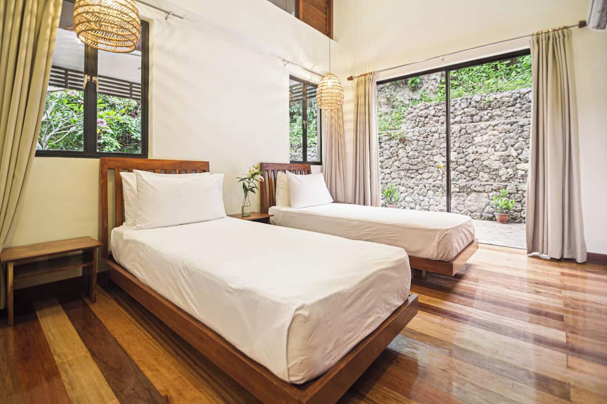 A bedroom with two beds, wooden flooring, and a stone wall visible through the window.