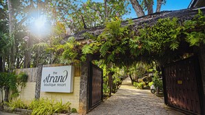 Entrada de un resort boutique con un sendero de piedra, una señal y abundante vegetación.