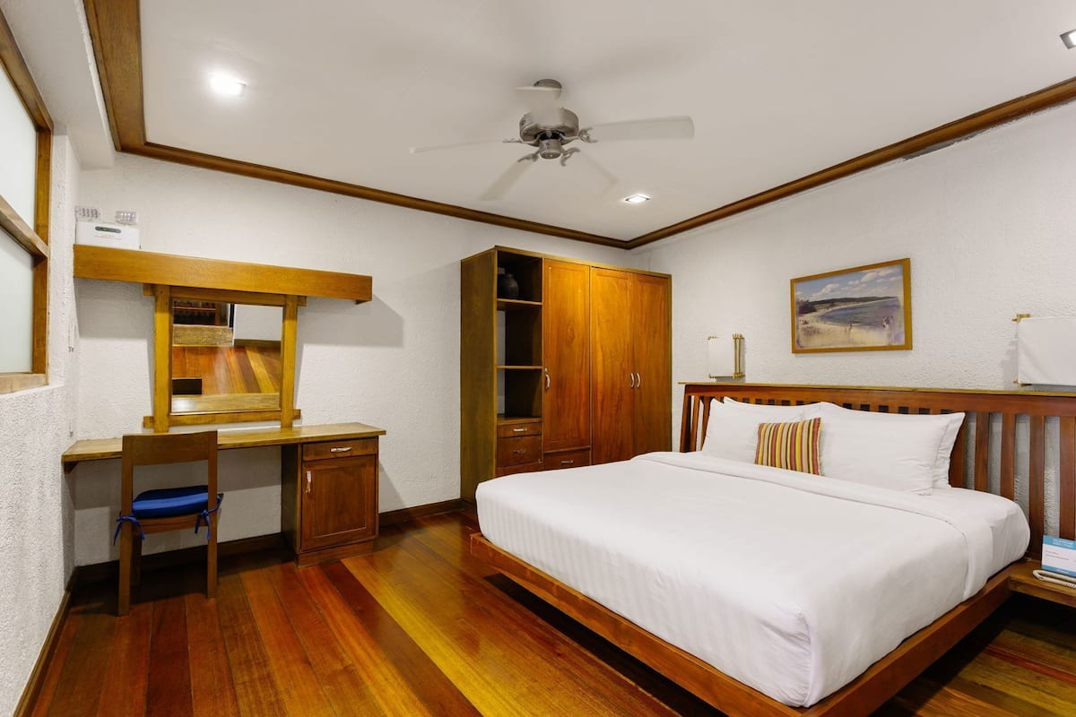 A bedroom with a wooden bed, a desk with a chair, a wardrobe, and a ceiling fan.