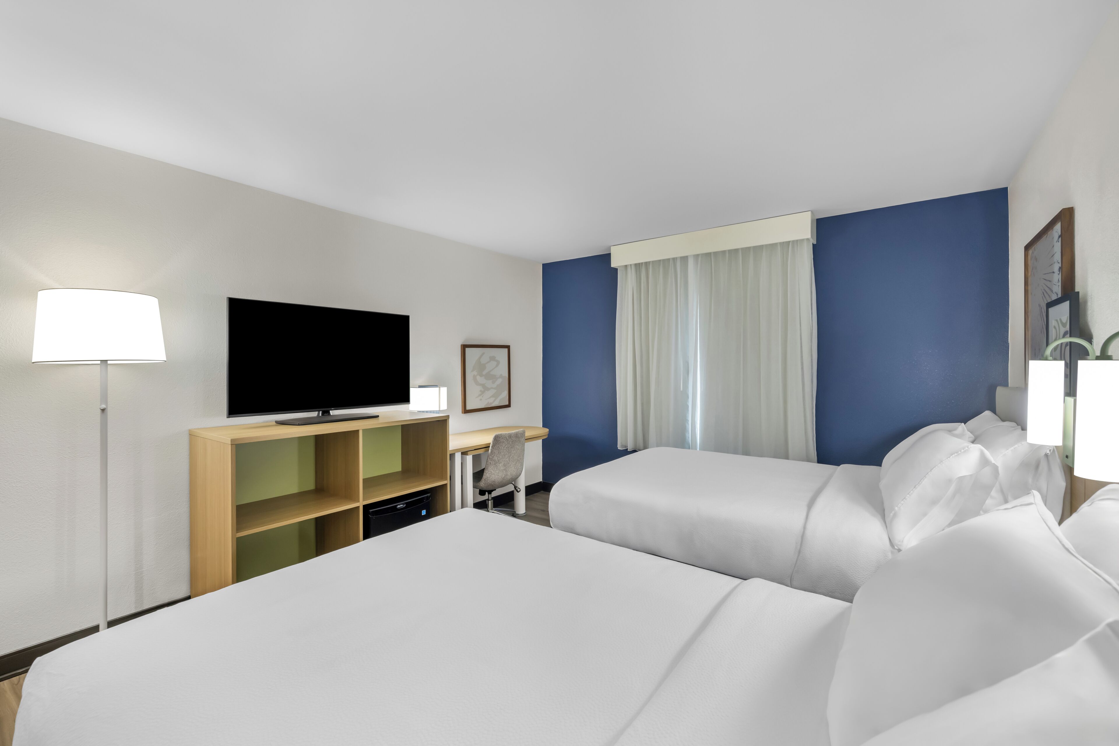 Ein Hotelzimmer mit Bett, Schreibtisch, Fernseher und einem Fenster mit Vorhängen.