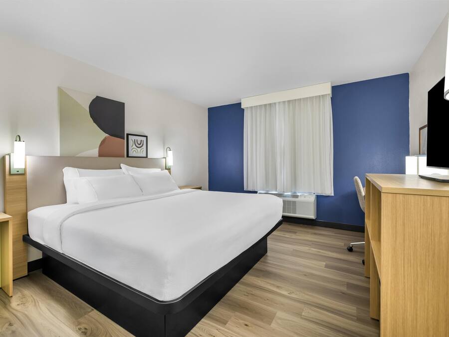 A modern hotel room with a large bed, bedside tables, a desk, and a window with curtains.