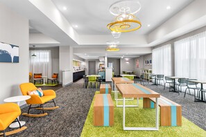 Una hall moderna di un hotel con zona ristorazione, posti a sedere e una cucina sullo sfondo.