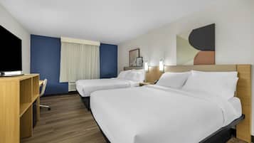 Ein Hotelzimmer mit zwei Betten, einem Schreibtisch, einem Stuhl und einem Fernseher.