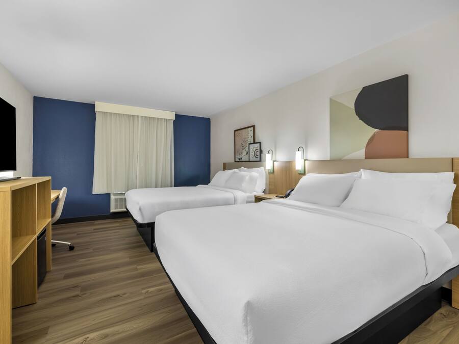 Ein Hotelzimmer mit zwei Betten, einem Schreibtisch, einem Stuhl und einem Fernseher.