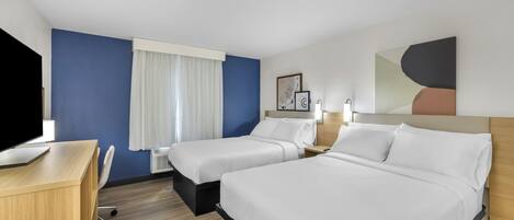 A hotel room with two beds, a desk, a chair, and a TV.