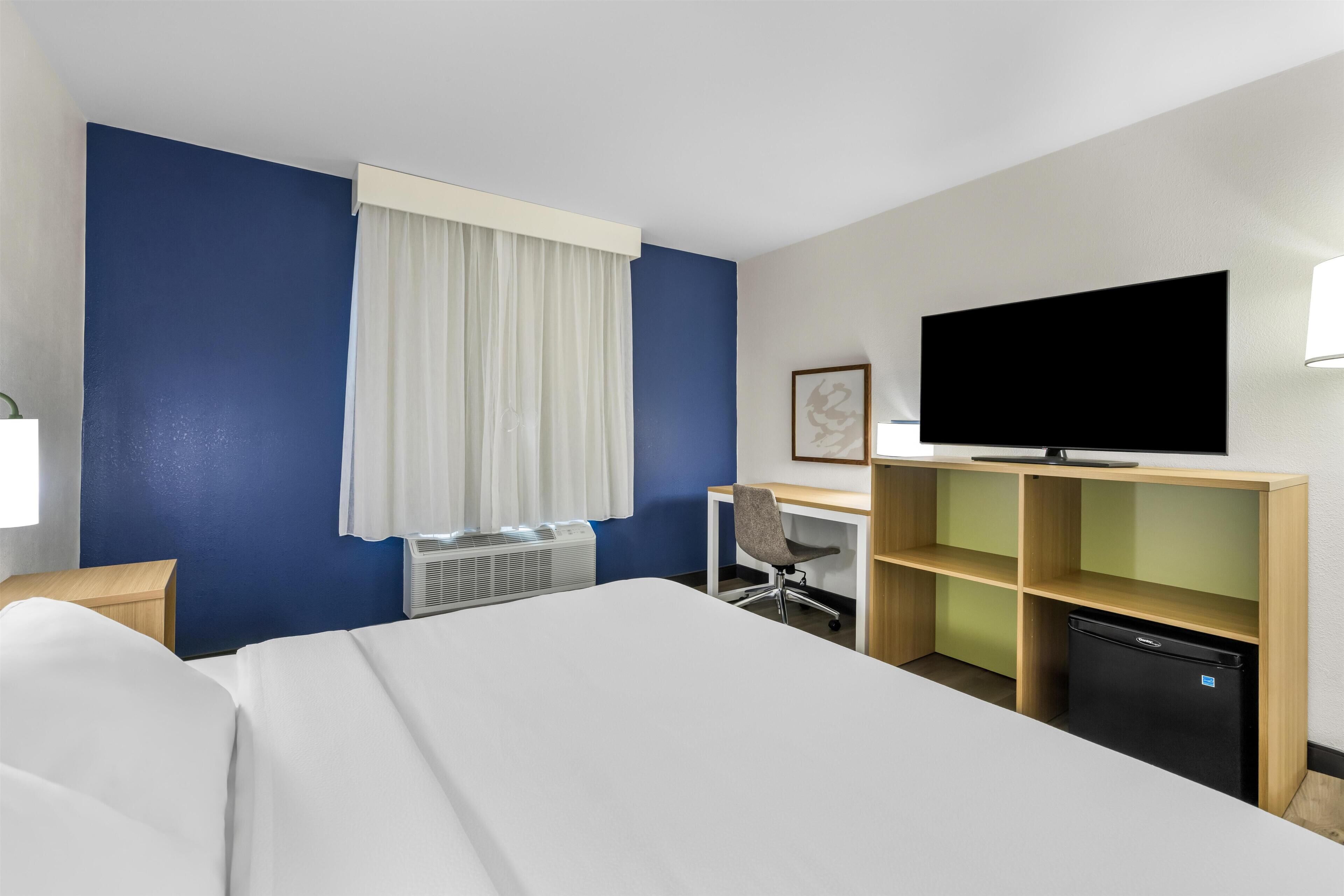 A hotel room with a bed, desk, chair, television, and a small refrigerator.