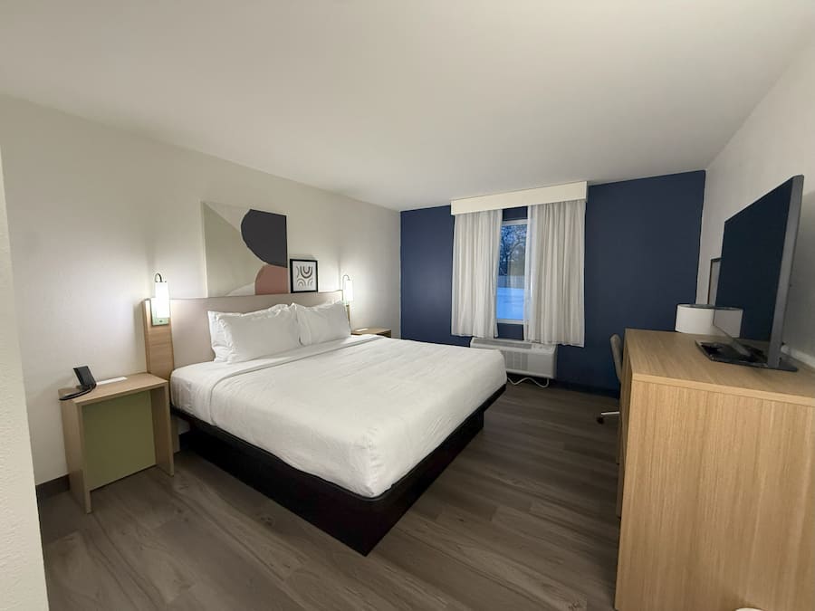 A hotel room with a large bed, bedside tables, a desk, and a window with curtains.