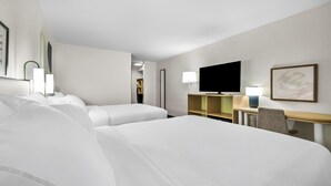 Ein Hotelzimmer mit zwei Betten, einem Schreibtisch, einem Stuhl, einem Flachbildfernseher und einer Lampe.