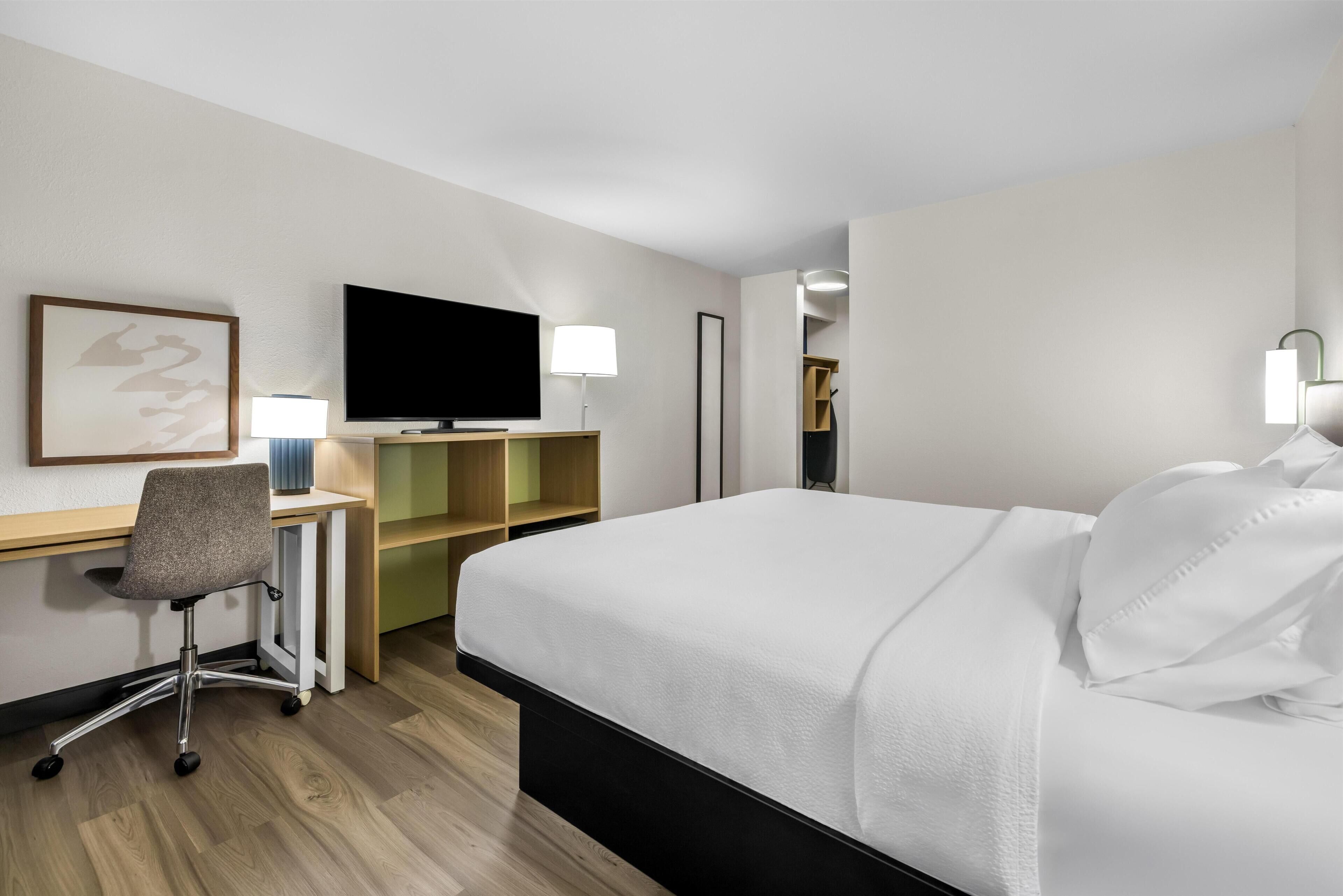 Ein Hotelzimmer mit Bett, Schreibtisch, Stuhl, Fernseher und Lampen.