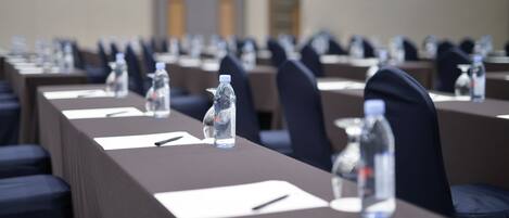 A conference room with rows of tables, each equipped with water bottles, nameplates, and pens.