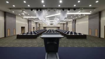 Een congrescentrum met rijen tafels en stoelen, plafondprojectoren en inbouwverlichting.