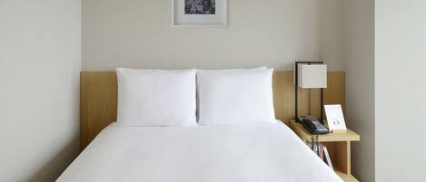Una cama bien hecha con sábanas blancas, un cabecero de madera, una mesita de noche con una lámpara y un cuadro en la pared.