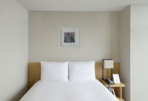 A neatly made bed with white linens, a wooden headboard, a bedside table with a lamp, and a framed picture on the wall.