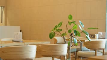 A restaurant interior with wooden tables and chairs, a menu stand, and a potted plant.