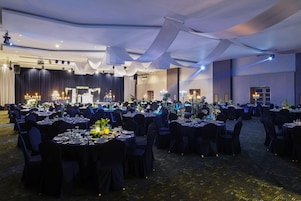 A banquet hall with round tables set for a formal event, featuring a stage and lighting equipment.