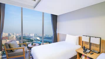 A hotel room with a large bed, a chair, a small table, and a nightstand with a lamp and phone.