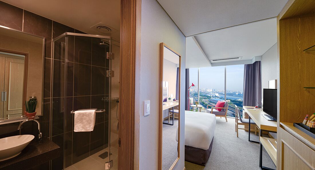 Habitación de hotel con baño, cama, escritorio y vistas a la ciudad.