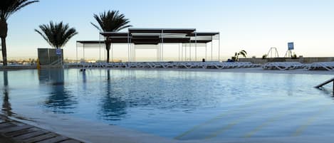 Una piscina al aire libre, sombrillas, sillones reclinables de piscina