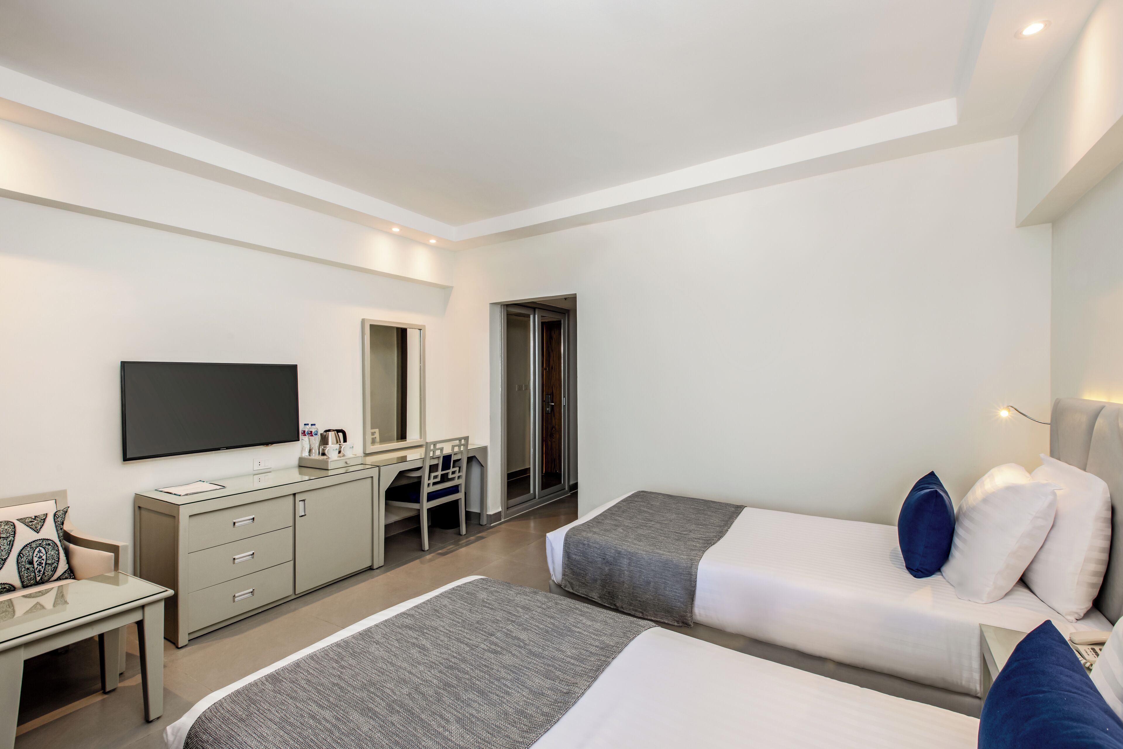 A modern hotel room with two beds, a desk, a flat-screen TV, and a wardrobe.