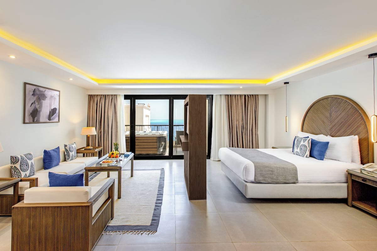 Quarto de hotel moderno com cama, escrivaninha, cadeira, sofá e varanda com vista.