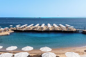Una località balneare con diverse sdraio e ombrelloni, un molo che si protende verso il mare e acque cristalline blu.