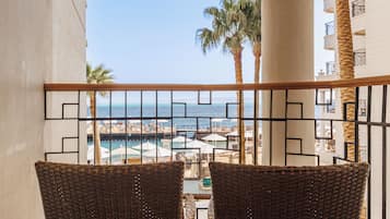 Un balcon avec des fauteuils en osier donnant sur une vue de la plage, des palmiers et une zone avec piscine.