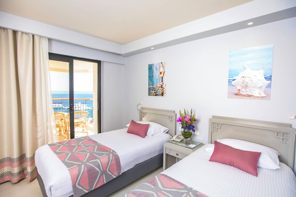 Quarto de hotel com duas camas, varanda com vista para o mar e obras de arte nas paredes.