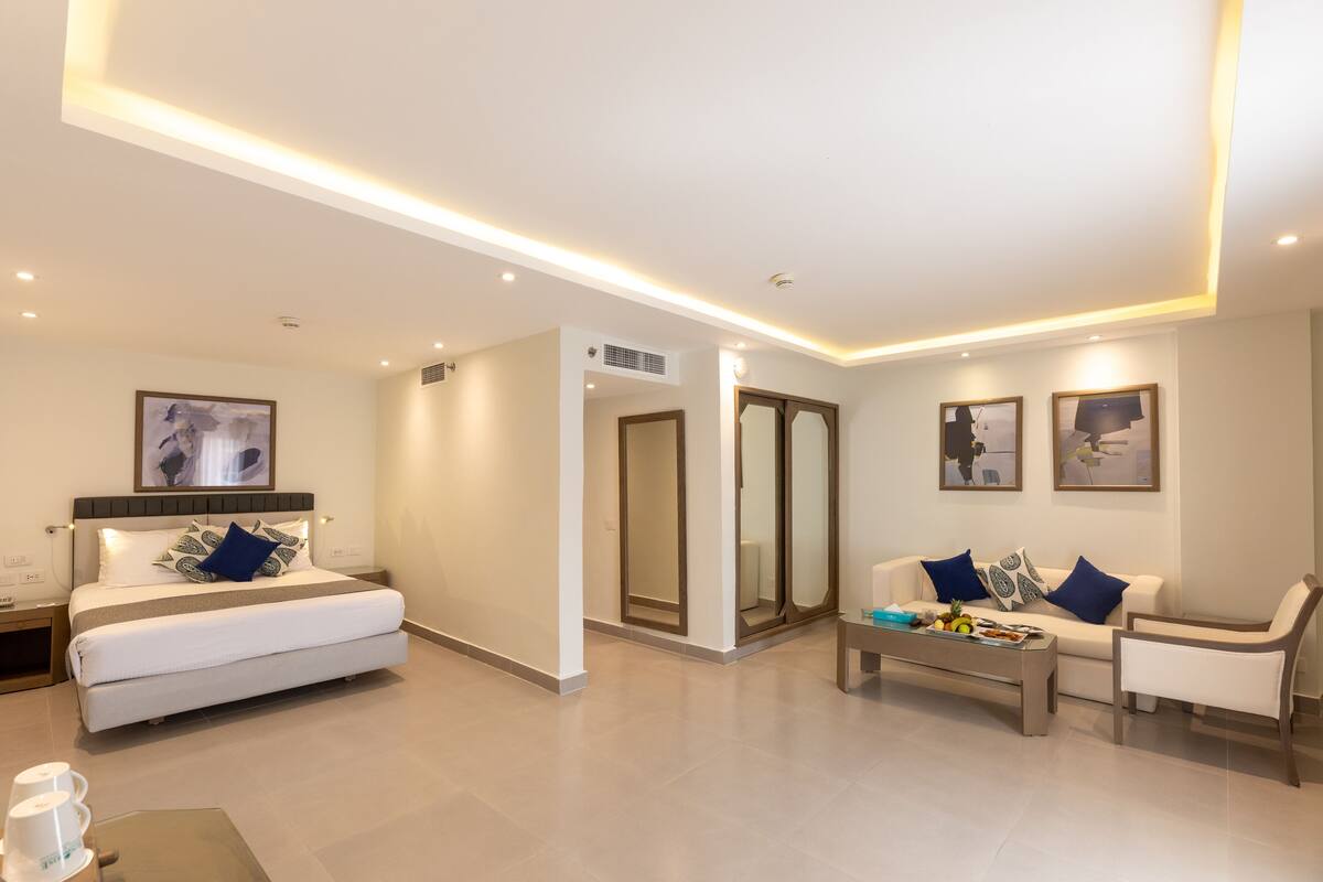 Quarto de hotel moderno com cama, sofá, mesa de centro e obras de arte nas paredes.