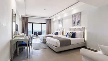 A modern hotel room with a large bed, a desk, and a view of the sea.