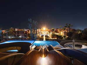 A nighttime view of a resort with a pool area, lounge chairs, and a water slide. - Aqualis Club Resort Marrakech - All Inclusive (Marrakech)