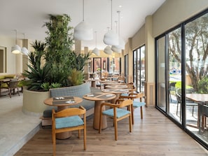 A modern dining area with round tables, wooden chairs, and hanging pendant lights. - Labranda Targa Club Aqua Parc (Marrakech)