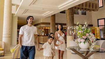 A family in a hotel lobby with a reception desk, seating area, and a decorative vase with flowers.