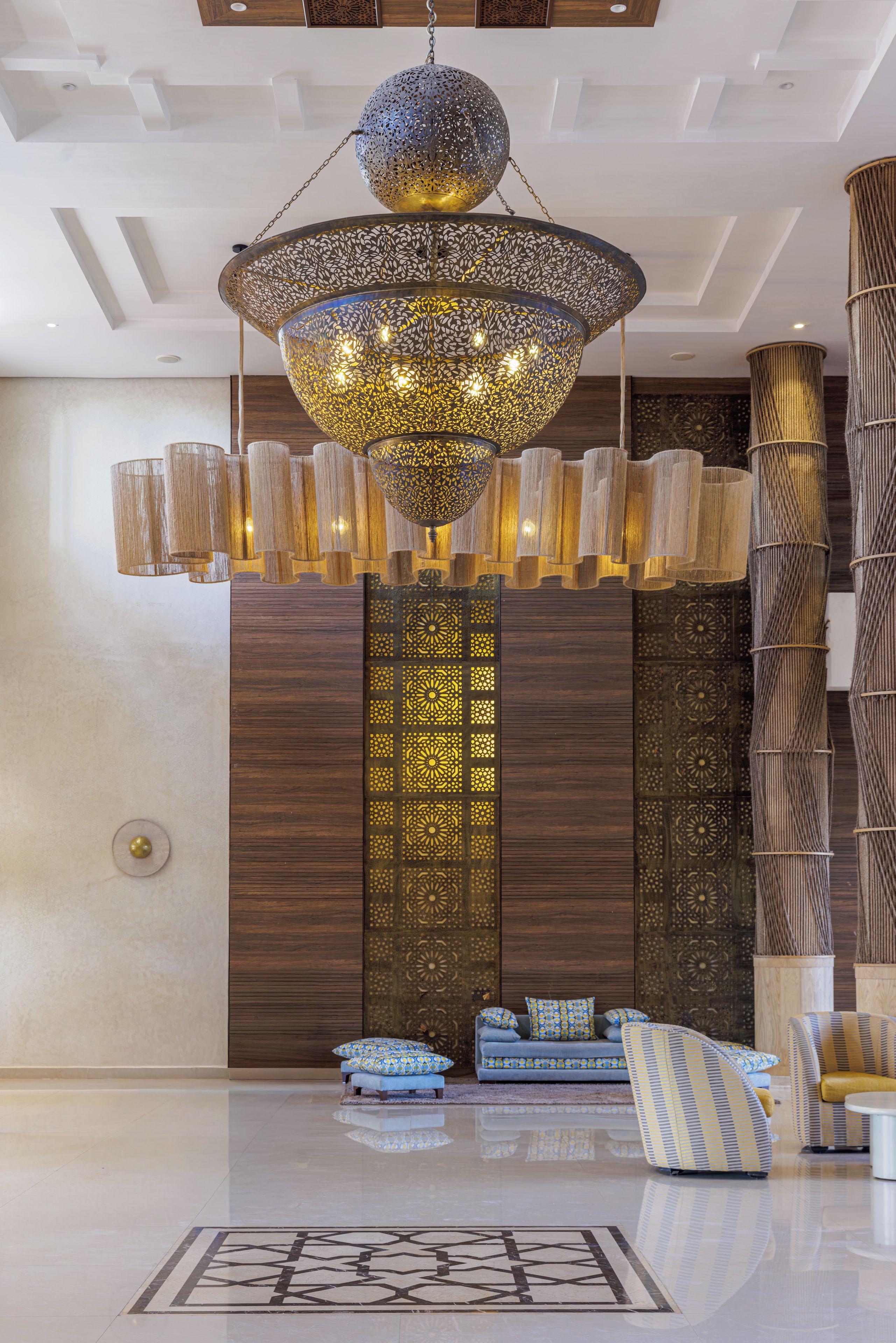 A modern lobby with a large chandelier, seating area, and decorative wall panels.